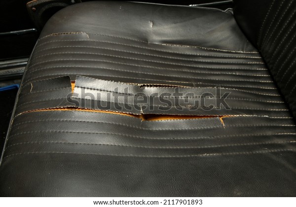 The black artificial leather  interior of the old\
classic car which needs a renovation. With destroyed ripped seat\
covers. 
