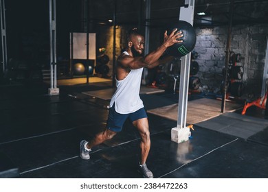 Black athlete standing and lifting heavy medicine ball in gym - Powered by Shutterstock