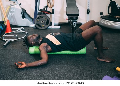 Black attractive strong man Doing an Exercise with Foam Roller on his Upper Back in a gym. Sport.
