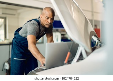 Black auto mechanic running diagnostic on laptop while analyzing engine problems in a workshop.  - Powered by Shutterstock