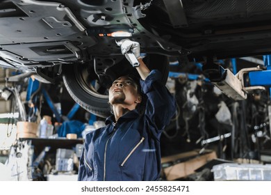 Black auto mechanic woman in overall and working gloves fixing car in auto repair garage - Powered by Shutterstock