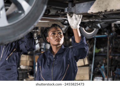 Black auto mechanic woman in overall and working gloves fixing car in auto repair garage - Powered by Shutterstock