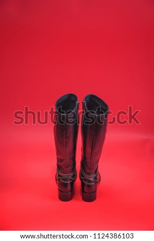 Black autumn boots on a red background. Winter shoes on a colored background. Spring shoes with high heels. Demi-season shoes