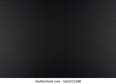 Black background made of real black paper with a matt fibrous structure, illuminated by a soft light on the sides..