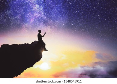 Black Backlit Young Guy Silhouette Sitting On Cliff Edge And Starry Night Sky Cosmos Background. Purpose And Way Concept 