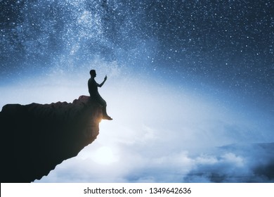 Black Backlit Young Guy Silhouette Sitting On Cliff Edge And Starry Night Sky Cosmos Background. Purpose And Success Concept 