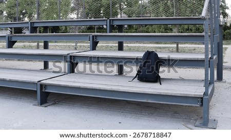 Black backpack forgotten on the bench in the schoolyard.
