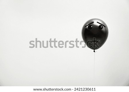 Black balloon with sad face on light grey background. Space for text