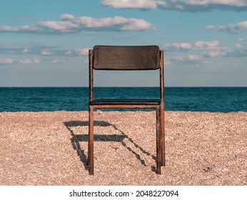 Black Beach Chair On Empty Sand Beach With Blue Sea Water Background. Minimalism Style Autumn Travel Relaxation, Spring Fall Vacation. No People, Nobody, Introversion Psychology Melancholia Depression