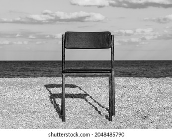 Black Beach Chair On Empty Sand Beach With Blue Sea Water Background. Minimalism Style Autumn Travel Relaxation, Spring Fall Vacation. No People, Nobody, Introversion Psychology Melancholia Depression