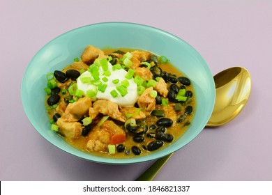 Black Bean Chicken Soup With Dollop Of Sour Cream In Blue Bowl With Golden Spoon On Lavender Background