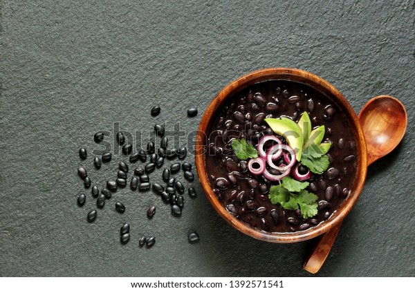  black bean soup or stew. Latin\
American or Mexican cuisine. stewed black beans served with avocado\
and red onion and cilantro. place for text. top\
view.