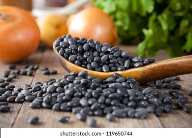 Black beans in a wooden spoon with cilantro and onions in the background