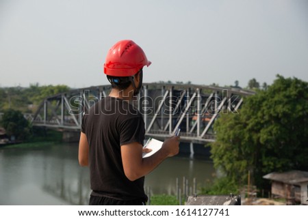 Black bearded engineer wear red hard hat and black working suit make decision and looking forward to iron bridge