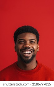 Black Bearded Young Man Smiling And Looking Upward Isolated Over Red Background