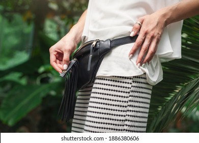 Black Belt Bag Fringe, Festival Leather Utility Belt, Custom Fanny Pack For Women. Women's Hands Demonstrate The Details Of The Bag. Green Tropical Plants Background.