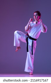 Black belt. Portrait of female taekwondo, karate athletes in doboks doing basic movements isolated on purple background in neon. Concept of sport, education, skills, martial arts, healthy lifestyle.