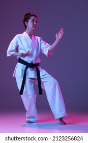 Black Belt. Portrait Of Female Taekwondo, Karate Athletes In Doboks Doing Basic Movements Isolated On Purple Background In Neon. Concept Of Sport, Education, Skills, Martial Arts, Healthy Lifestyle.
