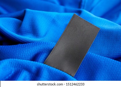 Black Blank Laundry Care Clothes Label On Blue Jersey Polyester Sport Shirt Background