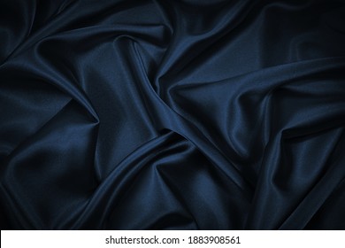 Black blue abstract background. Dark blue silk satin texture background. Beautiful wavy soft folds on the surface of the fabric. Navy blue elegant background with copy space for design. Web banner.