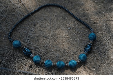 black and blue beaded necklace with round and textured shape, lies on sandy ground with dry twigs. - Powered by Shutterstock