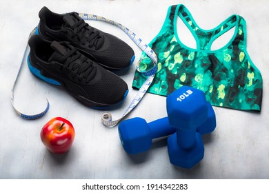 Black And Blue Tennis Shoes, Measuring Tape, Women's Sports Top, 10 Pound Weights And Red Apple On Gray Background.