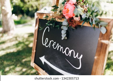 Black board with lettering 'Ceremony' stands on the path in the garden