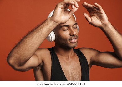 Black Bold Man Dancing While Listening Music With Headphones Isolated Over Brown Background