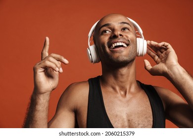 Black Bold Man Dancing While Listening Music With Headphones Isolated Over Brown Background