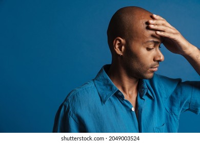 Black Bold Man With Headache Rubbing His Forehead Isolated Over Blue Background