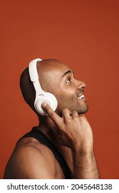 Black Bold Man Smiling While Listening Music With Headphones Isolated Over Brown Background