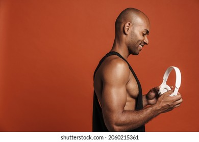 Black Bold Man Smiling While Posing With Headphones Isolated Over Brown Background