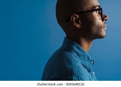 Black Bold Man Wearing Eyeglasses Posing In Profile Isolated Over Blue Background