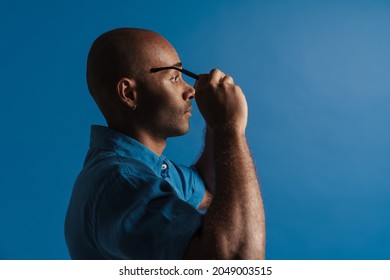 Black Bold Man Wearing Eyeglasses While Posing In Profile Isolated Over Blue Background