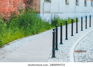 Black bollards lining an empty cobblestone sidewalk in an urban street