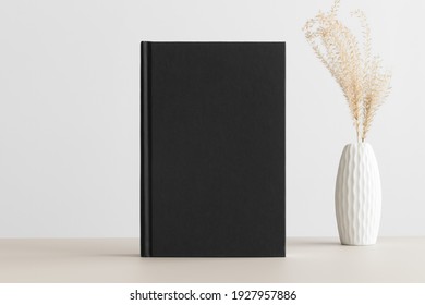 Black Book Mockup With A Dried Grass Decoration On A Beige Table.