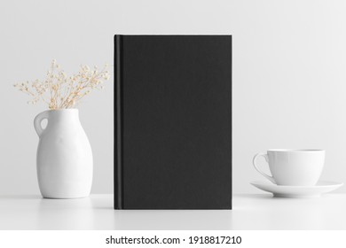 Black Book Mockup With A Gypsophila Decoration And A Cup Of Coffee On A White Table.