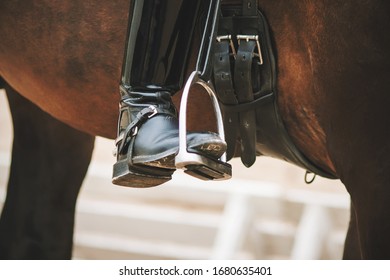 The black booted rider's foot bases on a metal stirrup, which is worn as a sporting gear on a Bay horse.