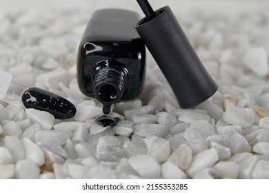 A Black Bottle Of Black Lacquer Lies Open On White Stones And Pours Down