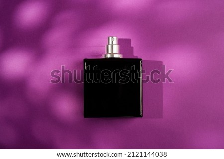 Black bottle of perfume on a purple background. Fragrance presentation with daylight. Trending concept with beautiful shadow. Women's essence.