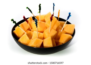 A Black Bowl Of Cubed Cantaloupe Melon With Party Toothpicks Isolated On White