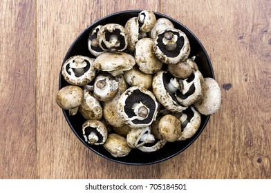 Black bowl on un-cooked mushrroms with wooden background