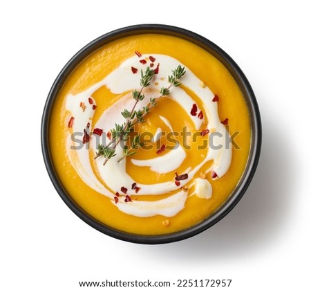 black bowl of vegetable cream soup decorated with thyme and chili flakes isolated on white background, top view