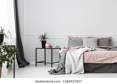 Black, Box Frame Side Table Next To A Cozy Bed With Gray Blankets And Pink Sheets In An Elegant Bedroom Interior