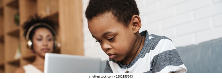 Black Boy Drawing And Sitting On Sofa While His Mother Working With Laptop At Home