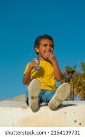 Black Boy Eating A Cookie With Chocolate. Walking Down The Street Dressed In A Yellow T-shirt, Smiling And Happy African-American Boy.