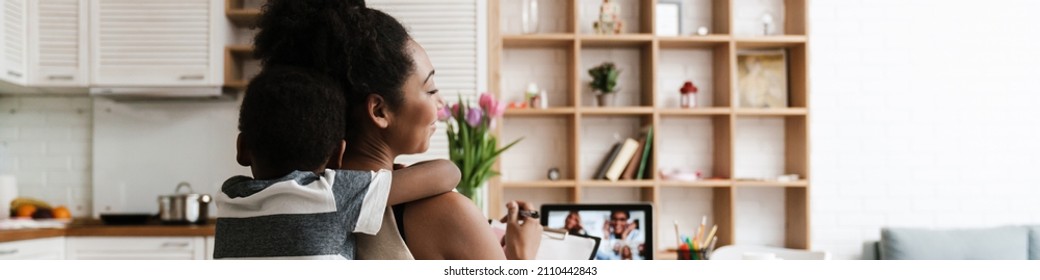 Black Boy Hugging His Mother While She Working With Laptop At Home