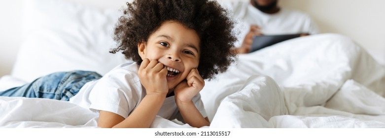 Black Boy Laughing While His Father Using Tablet Computer In Bed At Home