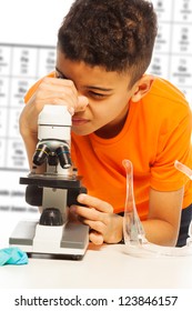 Black boy in orange looking in microscope on biology lesson