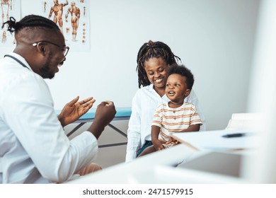 A black boy smiles during a medical exam, his mother beside him, as the doctor engages warmly, exemplifying child-friendly healthcare in a bright clinic. - Powered by Shutterstock